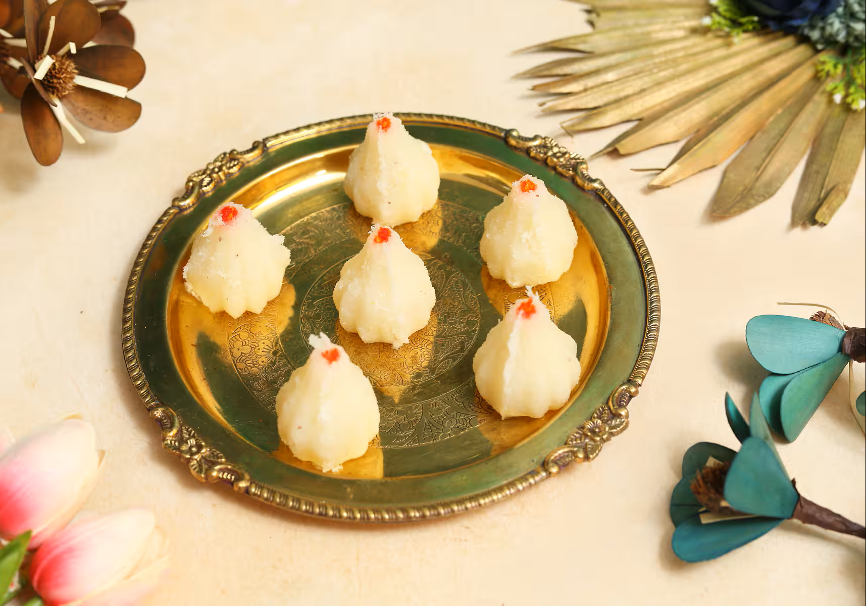 Six handmade coconut modaks on a brass plate with red garnish Nutty Ghee Sweets coconut modak in Gurgaon