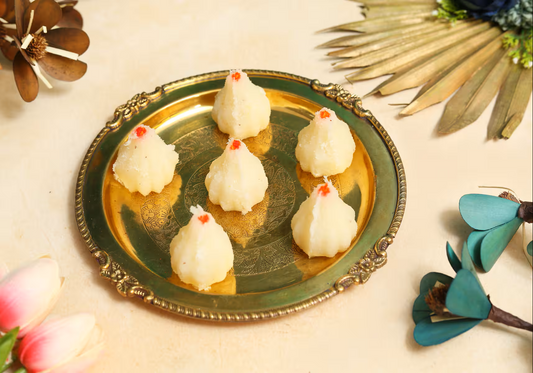 Six handmade coconut modaks on a brass plate with red garnish Nutty Ghee Sweets coconut modak in Gurgaon